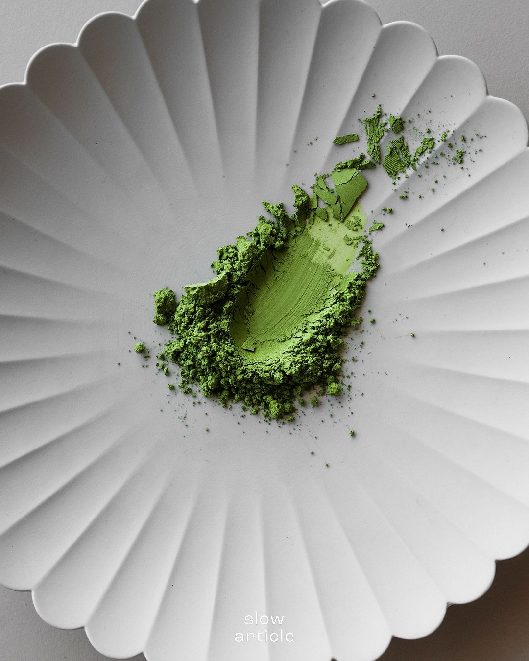 Bột matcha nguyên chất màu xanh đậm trên đĩa sứ trắng gợn sóng hoặc Cận cảnh bột trà xanh matcha chất lượng cao dùng trong pha chế.