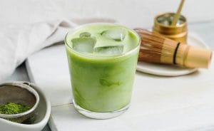 Ly matcha latte màu xanh nhạt đặt cạnh bột matcha và chổi tre pha trà